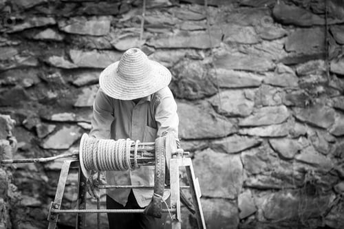 Preview: Man with straw hat working the hoist to get water in Asia in black and White