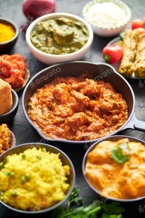 Preview: Various Indian dishes on a table. Spicy chicken Tikka Masala in iron pan