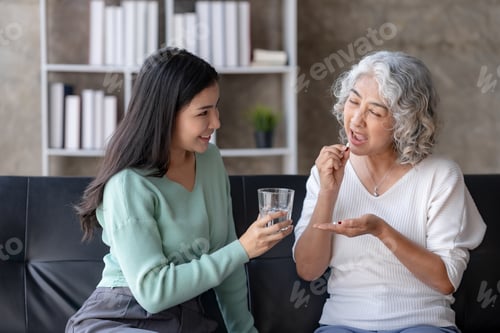 Preview: Asian elderly woman taking medicine for her ailments in the living room at home under the close supe
