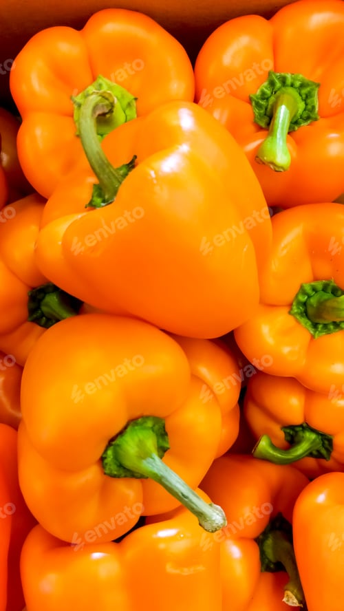 Preview: Closeup image of lots of red an orange bell peppers lying on counter in store