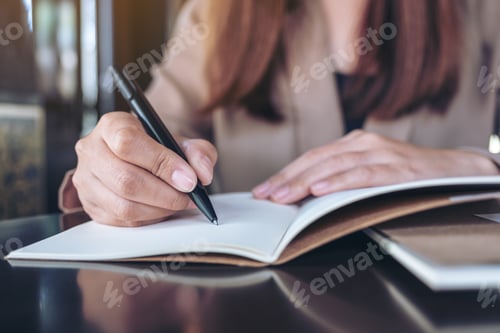 Preview: Closeup image of a business woman writing on blank notebook on wooden table