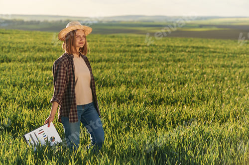 Preview: Growing season, green plants. Young woman is on the beautiful agricultural field at daytime