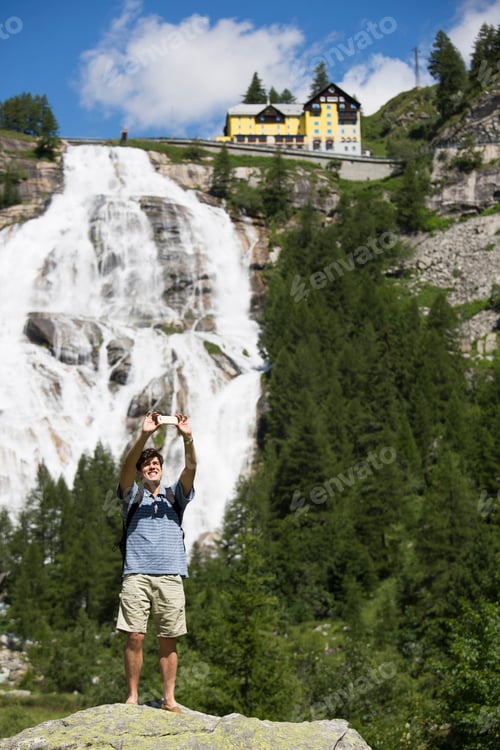 Preview: Young man taking smartphone selfie in front of Toce waterfall, Formazza, Verbania, Piemonte, Italy