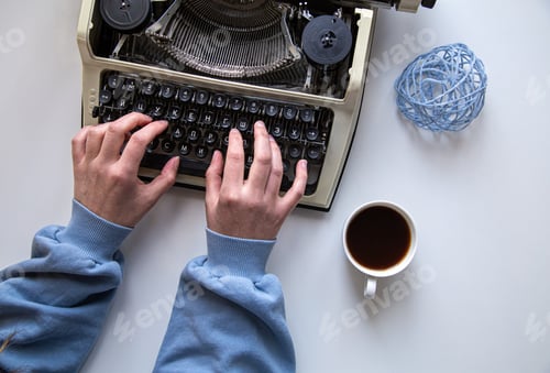 Preview: Woman's hand typing on a vintage typewriter top view.