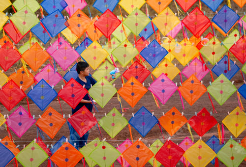 Preview: Asian boy enjoy to play bubble gun alone in area of row of kites outdoor and day light.