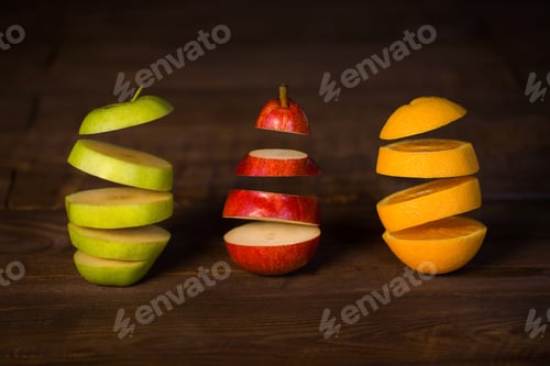 Preview: Apple, pear, orange cut in half frozen in the air on a black wooden background.