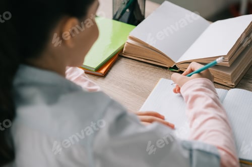 Preview: back view of schoolchild writing in notebook while sitting desk and doing homework