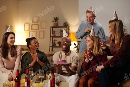 Preview: Happy young intercultural friends congratulating African guy on his birthday