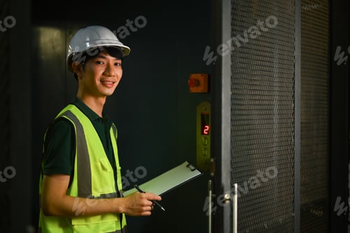 Preview: Asian male supervisor with clipboard standing in industrial plant and smiling to camera