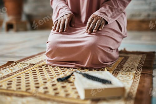 Preview: Unrecognizable Muslim woman kneeling on a prayer mat at home.