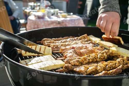Preview: Hot grill cheese is turned over with tongs, next to it lies meat on sticks on the grate