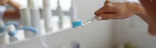 Preview: Close up of blue toothpaste on toothbrush in hand of Caucasian woman. Cleaning teeth.