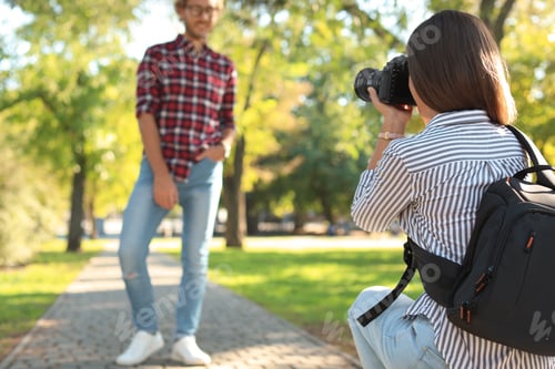 Preview: Young female photographer taking photo of man with professional camera in park