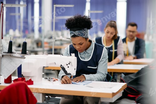 Preview: Young black woman working as seamstress at production line in textile factory.