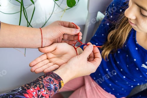 Preview: The mother ties a red thread to the child hand. Selective focus.