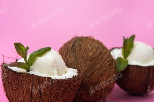 Preview: Vanilla ice cream balls in fresh coconut halves decorated with mint leaves on a pink background
