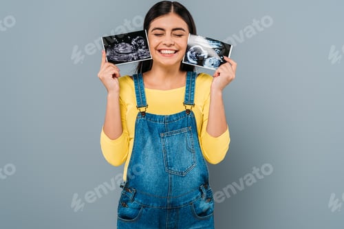 Preview: happy pregnant pretty girl holding fetal ultrasound images isolated on grey