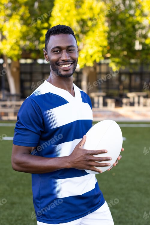 Preview: African American young male athlete holding a rugby ball, smiling at camera, copy space