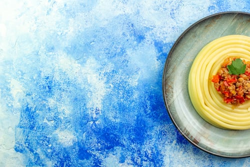 Preview: Overhead view of dinner with delicious spagetti on a gray plate on the left side on blue background