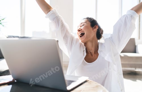 Preview: Happy woman with laptop raising arms in victory gesture