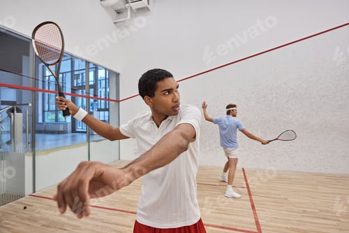 Preview: young interracial players in active wear playing squash together inside of court, lifestyle