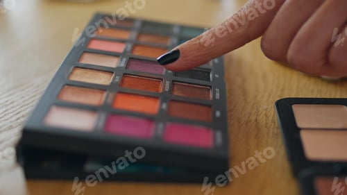 Preview: Woman finger pointing makeup palette at home close up. Girl taking eye shadows