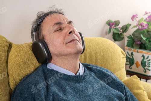 Preview: Senior man relaxing on couch with headphones, enjoying music