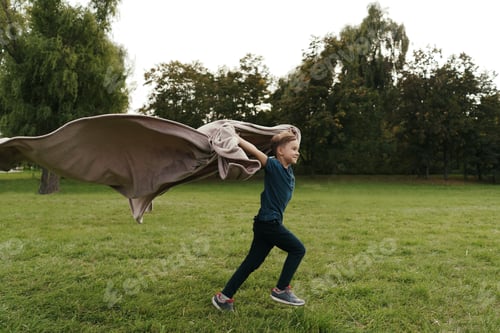 Preview: Cheerful boy running with a flying blanket in the park