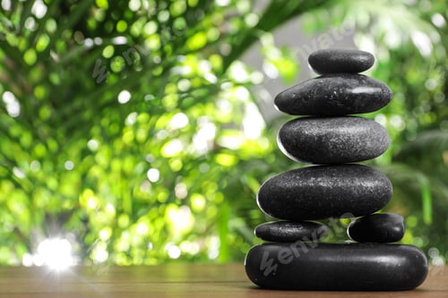 Preview: Table with stack of stones and blurred green leaves on background, space for text. Zen concept