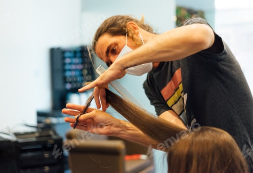 Preview: male hairdresser is cutting the ends of the hair of a woman with a protective mask