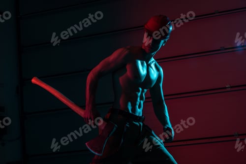 Preview: sexy shirtless fireman in protective hardhat holding flat head axe in darkness