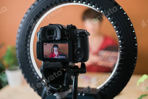 Preview: Middle-aged female beauty blogger or influencer with makeup product recording video in room at home