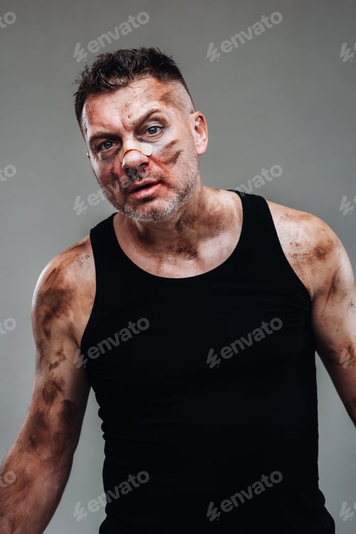 Preview: a battered man in a black T shirt who looks like a drug addict and a drunk stands against a gray