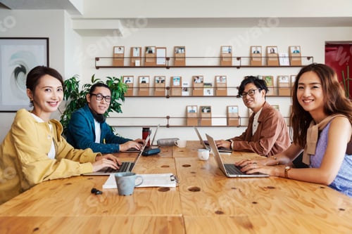 Preview: Group of young Japanese professionals working on laptop computers in a co-working space.