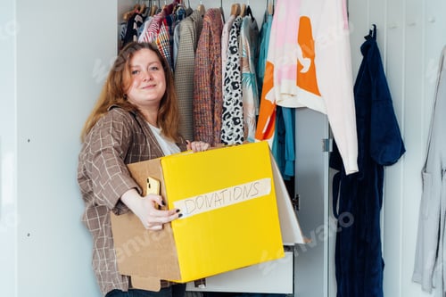 Preview: Smiling Woman with box of selected clothes from her wardrobe for donating to a Charity. Decluttering