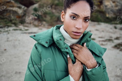 Preview: Beautiful serious African American girl in down jacket intently looking in camera posing outdoor
