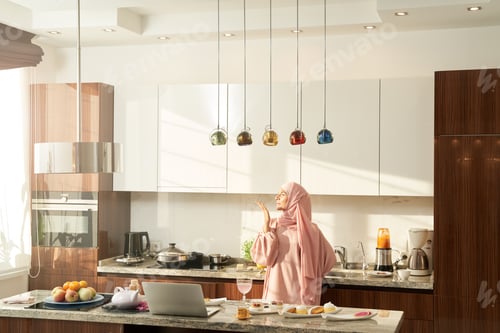 Preview: Islamic Arab woman sending air kiss in modern kitchen