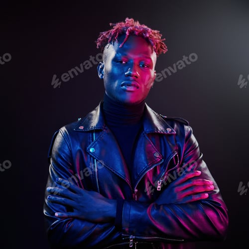 Preview: Futuristic neon lighting. Young african american man standing in studio with arms crossed