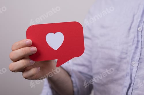 Preview: Sign of the heart in a text box made of red paper in the hands of a man