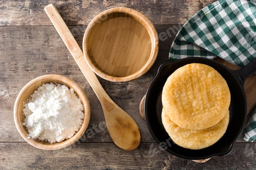 Preview: Delicious arepas in frying pan with precooked corn flour and wooden utensils