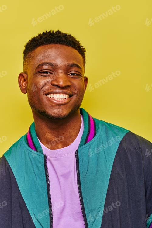 Preview: portrait of cheerful african american man in trendy windbreak jacket smiling at camera on yellow