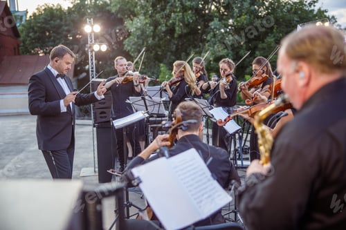 Preview: Conductor directing orchestra performance on outdoor stage