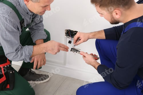 Preview: Senior electrician helping trainee stripping wire ends indoors