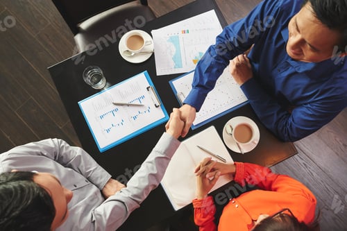 Business Colleagues Handshake Over Table with Charts