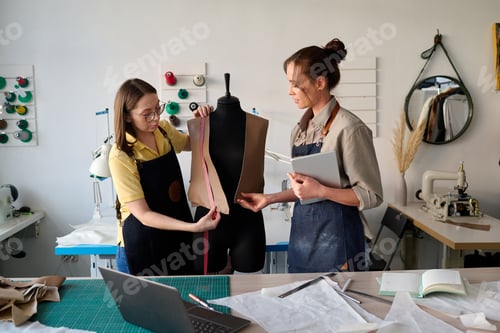 Preview: Young subordinate of tailor helping her with taking measures of waistcoat