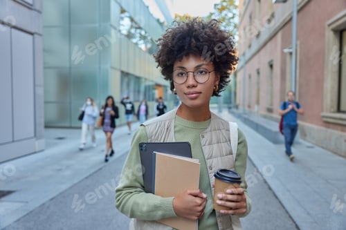Preview: Outdoor shot of pensive curly Afro American student going to university drinks takeaway coffee holds