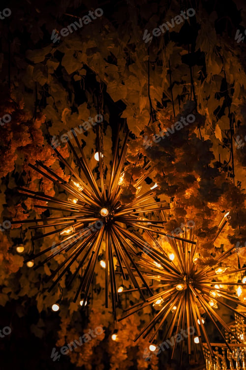 Preview: Vertical shot of shiny chandeliers hanging on a ceiling surrounded by floral decorations