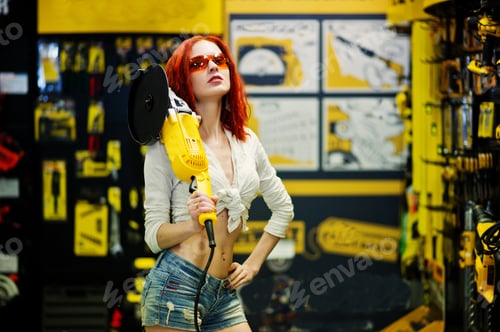 Preview: Red haired model posed with large angle grinder at store or household shop of working tools.