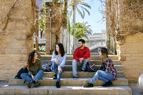 Preview: Four happy friends sitting on stairs outdoors talking