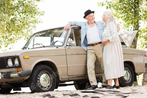 Preview: bottom view of stylish senior couple standing near beige vintage car and looking at each other
